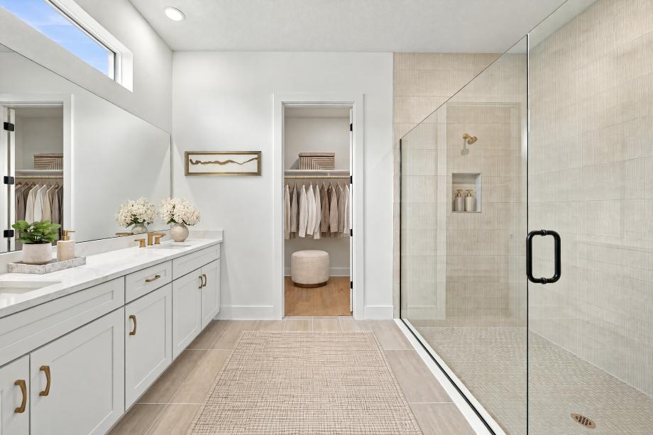 Luxurious primary bath with dual-sink vanity, glass-enclosed shower, and walk-in closet access