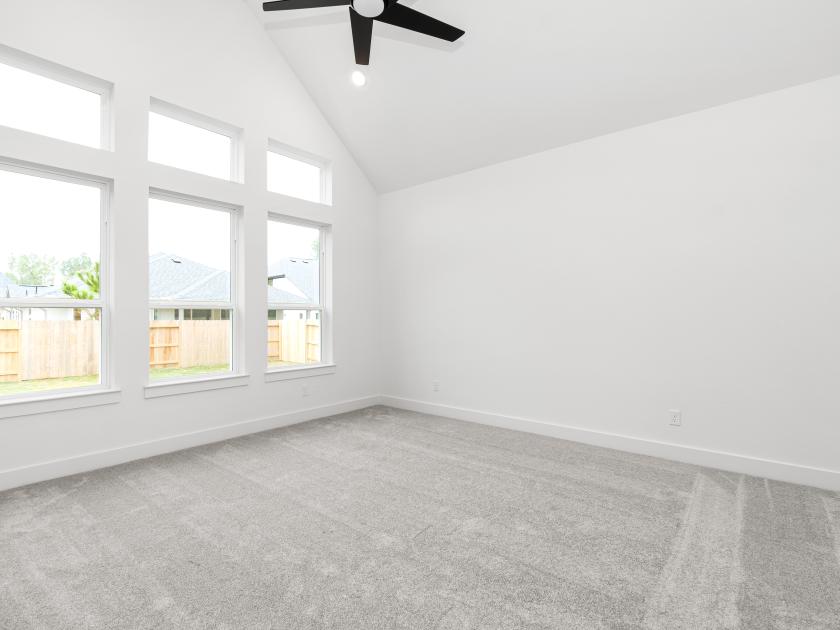 Spacious primary bedroom retreat with plush carpet, vaulted ceiling and backyard views